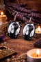 A curated collection of witchy-inspired acrylic earrings featuring dark, mystical designs including celestial symbols, occult figures, crystal shapes, and gothic motifs. Each pair showcases bold black detailing paired with soft lavender accents, displayed in styled scenes with crystals, candles, and moody textures. The collection blends alternative fashion with mystical aesthetics, creating a cohesive, edgy yet feminine visual