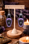 A curated collection of witchy-inspired acrylic earrings featuring dark, mystical designs including celestial symbols, occult figures, crystal shapes, and gothic motifs. Each pair showcases bold black detailing paired with soft lavender accents, displayed in styled scenes with crystals, candles, and moody textures. The collection blends alternative fashion with mystical aesthetics, creating a cohesive, edgy yet feminine visual