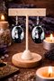 A curated collection of witchy-inspired acrylic earrings featuring dark, mystical designs including celestial symbols, occult figures, crystal shapes, and gothic motifs. Each pair showcases bold black detailing paired with soft lavender accents, displayed in styled scenes with crystals, candles, and moody textures. The collection blends alternative fashion with mystical aesthetics, creating a cohesive, edgy yet feminine visual