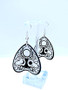 Collection of Ouija planchette acrylic earrings displayed in multiple design variations on a clean background. Each pair features unique lettering styles, symbols, and finishes while maintaining a cohesive dark, witchy aesthetic. The assortment highlights different options within the same occult-inspired theme.