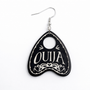 Collection of Ouija planchette acrylic earrings displayed in multiple design variations on a clean background. Each pair features unique lettering styles, symbols, and finishes while maintaining a cohesive dark, witchy aesthetic. The assortment highlights different options within the same occult-inspired theme.