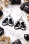 Collection of Ouija planchette acrylic earrings displayed in multiple design variations on a clean background. Each pair features unique lettering styles, symbols, and finishes while maintaining a cohesive dark, witchy aesthetic. The assortment highlights different options within the same occult-inspired theme.