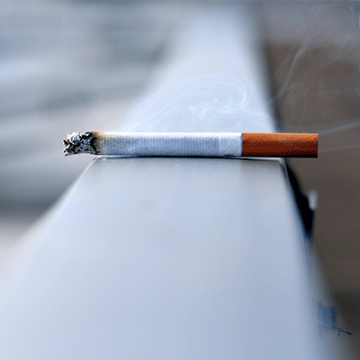 Lit Cigarette Balanced on a Ledge With Smoke Cloud