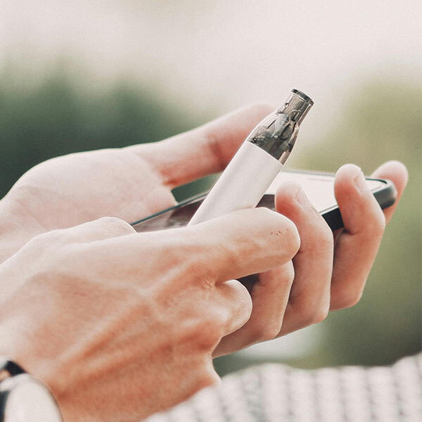 Person holding small vape while looking at phone