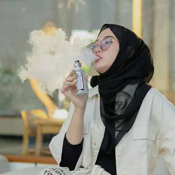 Woman smartly dressed holding and vaping a Sub-Ohm silver kit outdoors while sat down at a table. Woman vaping Sub-Ohm device outdoors