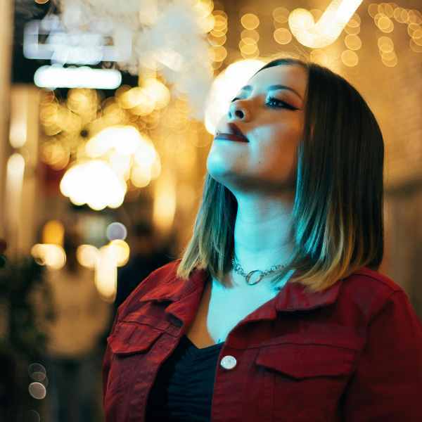 Woman with red jacket vaping outside, puffing a small amount of vapour. Woman vaping discreet clouds outside