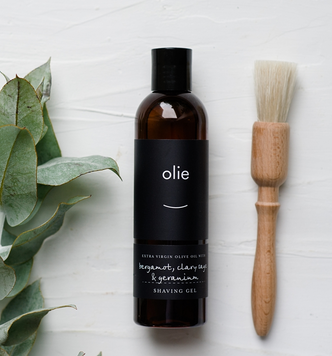 Olie shaving gel in bottle laying flat with wooden shave brush