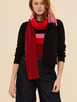 A model wearing the Long Play Scarf styled over a matching black knit top, demonstrating how the long, cozy scarf drapes and layers against a dark outfit.