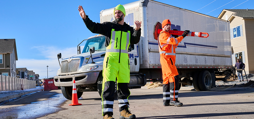 Two male transportation workers outside in the cold wearing high-visibility workwear.