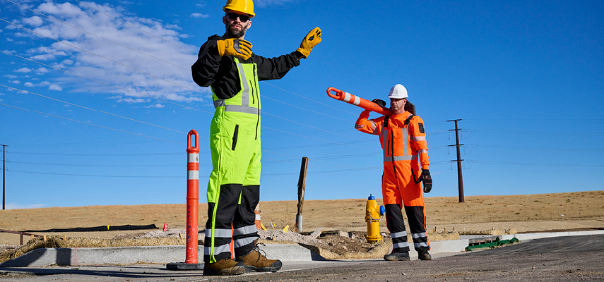 Two outdoor construction workers wearing hivis insulated workwear while directing traffic