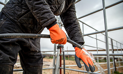 Man hosing off waterproof gloves after doing farm work