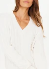 THE UPSIDE women's white Seymour Knit Sweater made with 100% organic cotton cable knit fabrication features a v-shaped neckline, ribbed cuffs, hem and neck, and embroidered arrow logo on back of neck.