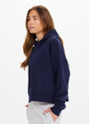 THE UPSIDE women's navy organic cotton Byron Embossed Logo Hoodie is designed for a relaxed boxy fit and features a tonal embossed horseshoe logo on the chest.