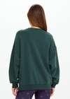 THE UPSIDE women's dark green Alumni Coolum Crew Neck Sweater is made from organic cotton and feature small side splits, front zip pocket and side pockets.