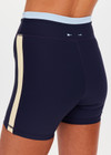 THE UPSIDE women's navy recycled nylon Hermosa 4 Inch Spin Short is mid rise and features a light blue stripe at upper waistband and pockets at the side. Made for yoga and pilates.