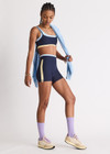 THE UPSIDE women's navy recycled nylon Hermosa 4 Inch Spin Short is mid rise and features a light blue stripe at upper waistband and pockets at the side. Made for yoga and pilates.