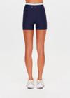 THE UPSIDE women's navy recycled nylon Hermosa 4 Inch Spin Short is mid rise and features a light blue stripe at upper waistband and pockets at the side. Made for yoga and pilates.