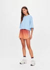 THE UPSIDE women's red recycled polyester Maya Billie Run Short is mid rise and features light blue mesh tape down side seams and side pockets. Made for running.