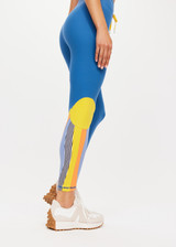 THE UPSIDE women’s blue mid-rise 25 Inch Midi Pant made with Recycled Peached fabric features a colour-block panelled sun feature on one leg, contrasting yellow elastic drawcord through waist and moisture wicking properties