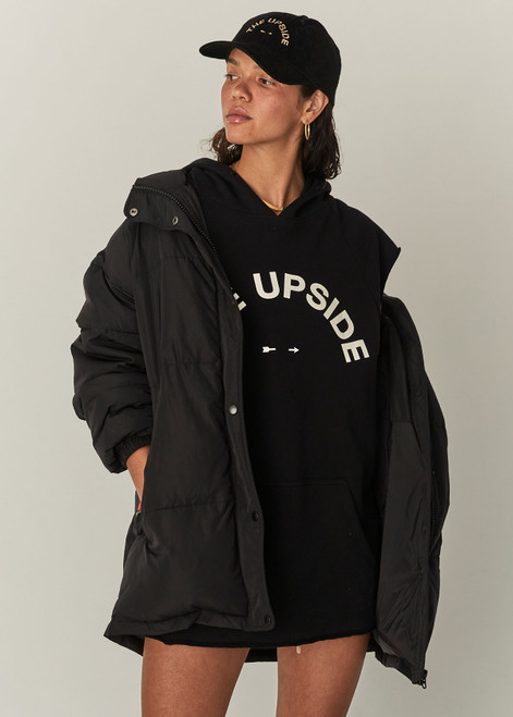 THE UPSIDE Recovery Hoodie in Black is an organic cotton sleeveless, longline hoodie with a cream horseshoe logo print at centre front and raw edges with kangaroo pocket and drawcord through hood.