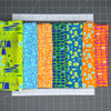 Brightly colored Modern Marks 7-pc fat quarter bundles available available Sit n' Sew Fabrics spread out on a cutting mat.