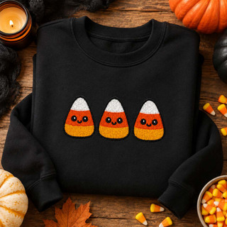 Three smiling candy corn embroidery designs stitched on a black sweatshirt