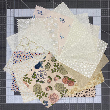 Assorted cream 5-inch fabric squares arranged on a cutting mat
