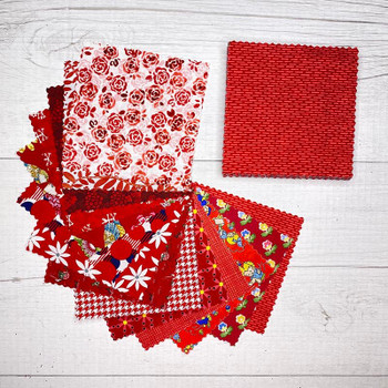 Assorted red 5-inch fabric squares arranged on a white wood background