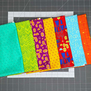 Bright colored fabrics from the Modern Marks collection of fabrics displayed all together on a cutting mat.