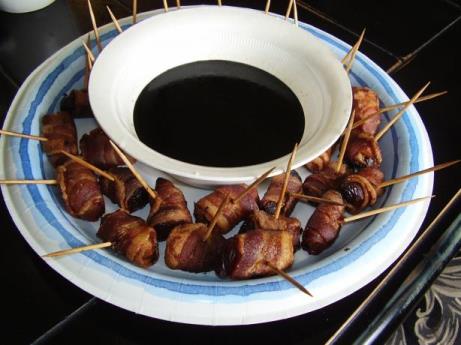 Bacon Apricot appetizers on skewers placed around a dipping sauce dish on a serving platter
