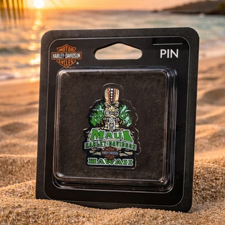 Maui Harley-Davidson Tiki Guy Pin in original packaging resting on a sandy beach at sunset