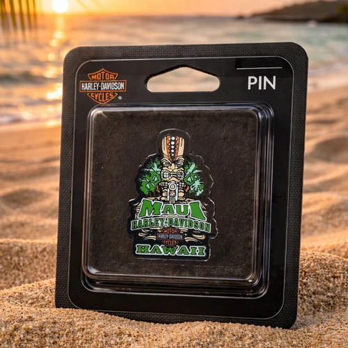 Maui Harley-Davidson Tiki Guy Pin in original packaging resting on a sandy beach at sunset