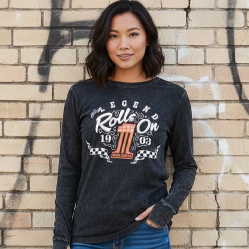 Front view of a woman standing against a brick wall wearing the black Harley-Davidson Women's Legend Rolls On Long Sleeve Tee