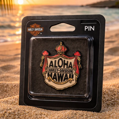 Harley-Davidson Coat of Arms Pin in original packaging resting on a sandy beach at sunset