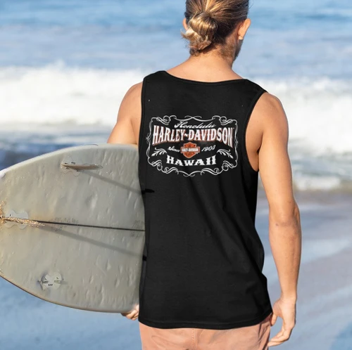 Man at the beach holding a surfboard wearing the Harley-Davidson Men's Vintage Art Black Tank Top featuring Honolulu H-D Hawaii graphic
