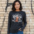 Front view of a woman standing against a brick wall wearing the black Harley-Davidson Women's Legend Rolls On Long Sleeve Tee