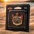 Harley-Davidson Coat of Arms Pin in original packaging resting on a sandy beach at sunset