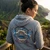 Back view of Nickel Harley-Davidson Women's Little Birdies Zip Up Hooded Jacket showing tropical blue birds and sunrise graphic