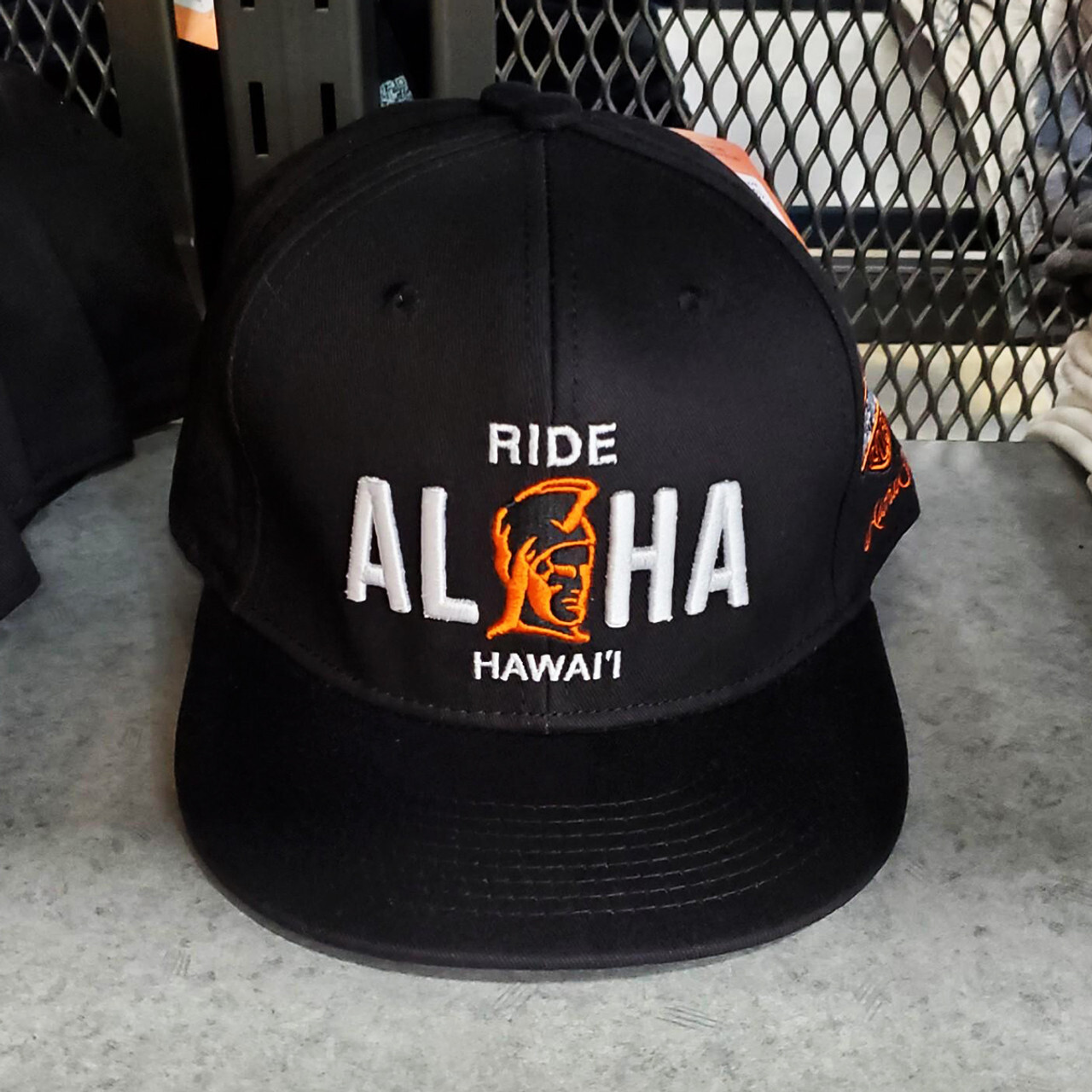 Harley-Davidson Ride Aloha Black Cap, a flat bill snapback hat featuring the white and orange 'RIDE ALOHA HAWAIʻI' graphic, a popular Hawaiian exclusive motorcycle souvenir.
