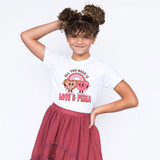 All You Need Is Love & Pizza DTF Heat Transfer, a girl wearing a white t-shirt with a cute graphic of love and pizza characters and the phrase, with a pink skirt, against a plain white background.