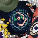 Dance Like Nobody's Watching Screen Print Heat Transfer, vibrant graphic design featuring a woman with dark hair in a dynamic dance pose surrounded by skulls and barbed wire, on a black fabric.