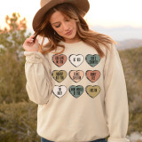 Blake Candy Hearts DTF Heat Transfer, woman wearing a cream sweatshirt adorned with colorful heart-shaped designs with sayings, outdoors at sunset.