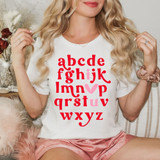 Vday Alphabet DTF Heat Transfer, colorful alphabet print with a pink heart on a white t-shirt worn by a woman with blonde hair.
