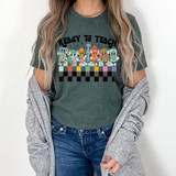Ready To Teach DTF Heat Transfer, colorful cartoon characters and text on a green T-shirt worn by a woman.