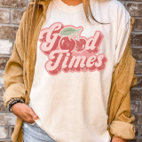 Good Times Cherry Screen Print Heat Transfer, pink cherry graphic with the words 'Good Times' in a retro font on a white T-shirt worn by a person standing against a brick wall.