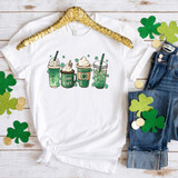 Lucky Lattes Sublimation Transfer, colorful St. Patrick's Day-themed design on a white T-shirt featuring four shamrock drinks with whipped cream and festive decorations.