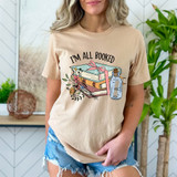 I'm All Booked DTF Heat Transfer T-shirt, women's beige t-shirt with a graphic design of books, flowers, and a bottle.