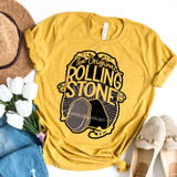 The Original Rolling Stone DTF Heat Transfer, yellow T-shirt with black graphic design of a stone and text, flat lay with accessories and white flowers.