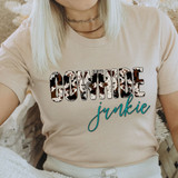 Cowhide Junkie DTF Heat Transfer, close-up of a beige T-shirt with cowhide pattern text and a teal cursive word 'junkie' printed on it.