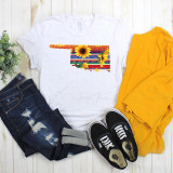 Serape Sunflower Oklahoma print Sublimation Transfer, white T-shirt featuring colorful Oklahoma state outline with sunflower and sunburst design, paired with distressed jeans, yellow pants, and black Vans sneakers.
